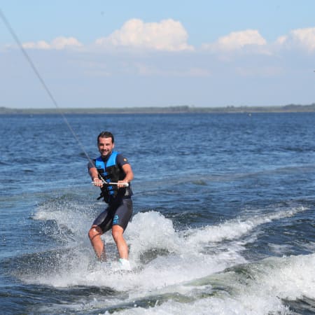 Pratiquant de wakeboard en action sur le lac de Carcans, tracté par un câble, gilet de sauvetage bleu, conditions calmes et ensoleillées