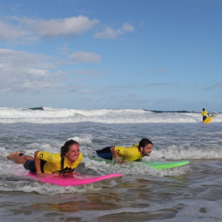 Moniteurs en gilets de sauvetage jaunes initiant des enfants au surf sur planches colorées dans l'océan avec vagues