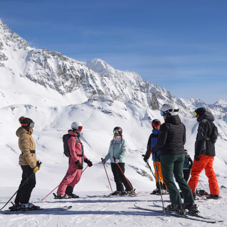 Groupe de skieurs et snowboardeurs sur piste enneigée face à massif montagneux enneigé en Vallée de la Guisane