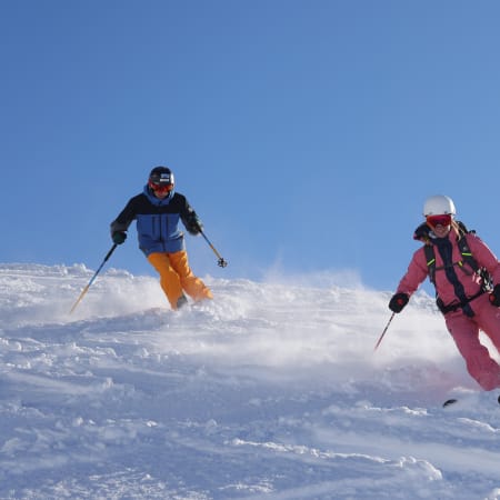 Deux skieurs descendant une piste enneigée sous un ciel bleu aux Pyrénées pendant un séjour ski mi-temps