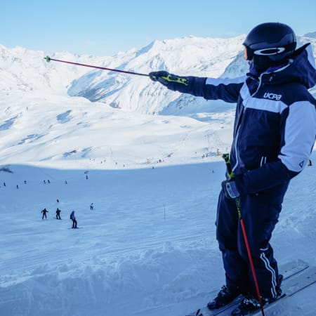 Skieur hors piste aux Deux-Alpes levant les bras face aux pentes enneigées et montagnes alpines