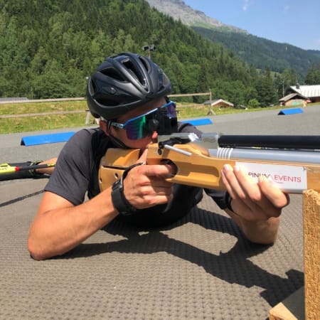 Athlète en biathlon tenant un fusil de tir couché avec montagne et forêt en arrière-plan