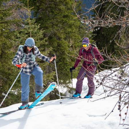 Deux skieurs en randonnée montant une pente enneigée dans une forêt alpine du Mont-Blanc avec équipement de ski hors-piste