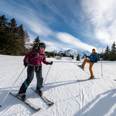 Trois skieurs en action sur une piste enneigée avec montagnes enneigées et forêts de sapins en arrière-plan