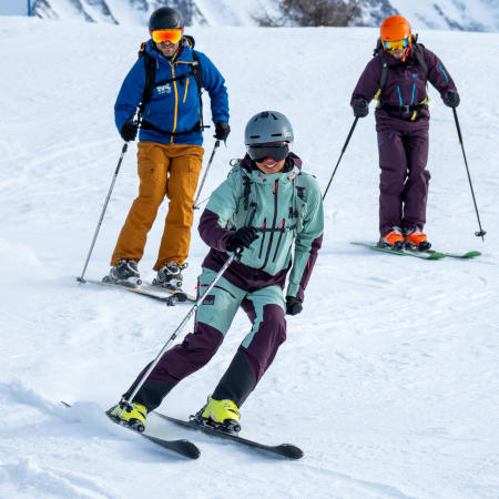 Trois skieurs en équipement coloré descendant une piste enneigée de Saint Lary avec montagnes en arrière-plan