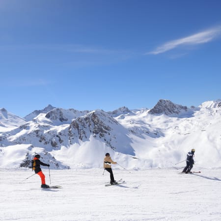 Groupe de skieurs en progression sur piste enneigée avec massif montagneux enneigé de Serre Chevalier en arrière-plan