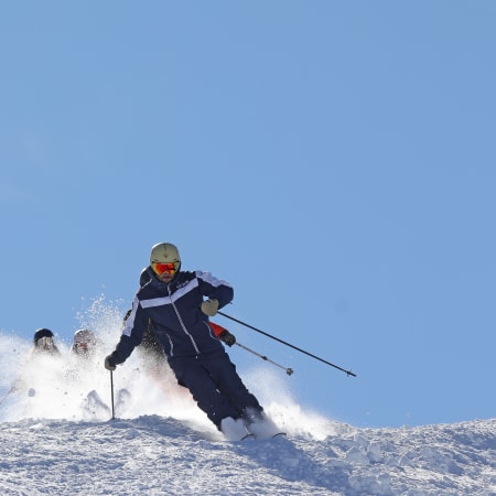 Skieur dévale une pente enneigée à Serre Chevalier sous un ciel bleu dégagé, projection de poudreuse blanche