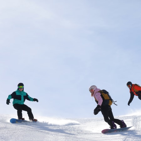 Trois skieurs et snowboardeurs en action sur les pistes enneigées de Val d'Isère sous un ciel dégagé