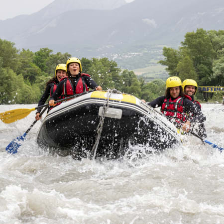 Groupe de jeunes en rafting sur eaux vives avec casques et gilets de sauvetage, montagnes verdoyantes en arrière-plan