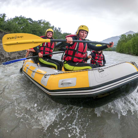 Groupe de rafters en gilet de sauvetage rouge et jaune naviguant en raft sur une rivière en montagne lors d'une activité Multisport Audace