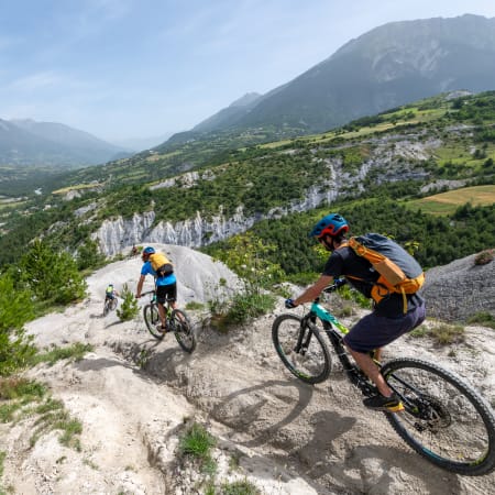 Cyclistes en vélo de montagne sur sentier rocheux avec vue panoramique sur vallée alpine verdoyante et falaises calcaires