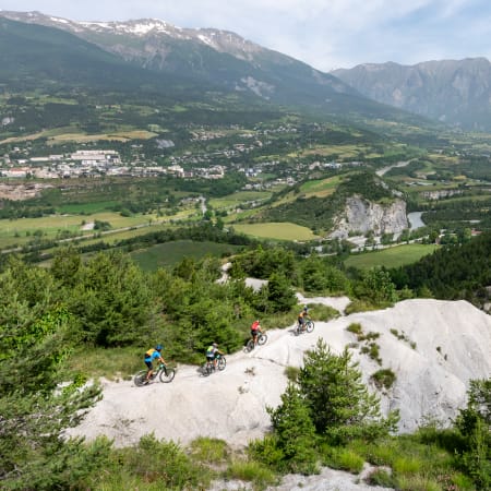 VTT au pays de Serre Ponçon avec cyclistes sur plateau rocheux dominant la vallée verdoyante et les massifs montagneux
