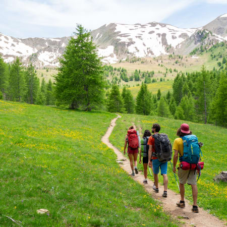 Groupe de randonneurs sur sentier alpin près du lac de Serre-Ponçon avec montagnes enneigées et forêt de sapins
