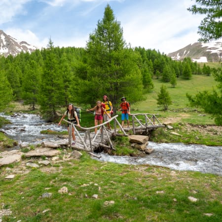 Groupe de randonneurs traversant un ruisseau de montagne en altitude avec sommets rocheux et forêt de mélèzes