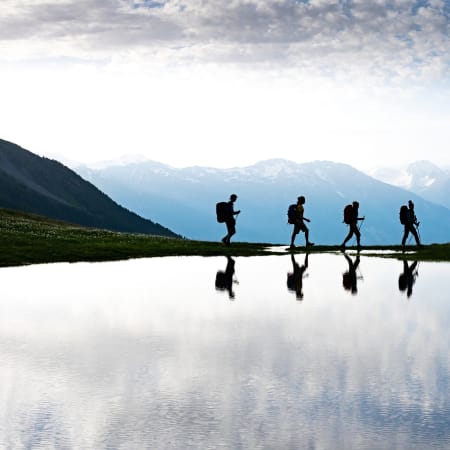 Groupe de randonneurs en itinérance dans les Écrins avec sommets enneigés et lac alpin en réflexion