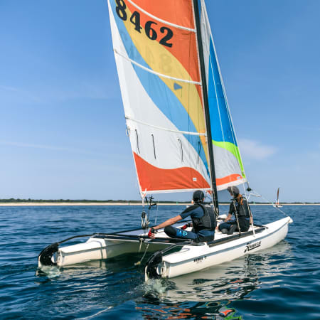 Dériveur avec voile colorée et moniteur en initiation nautique sur mer calme et ensoleillée