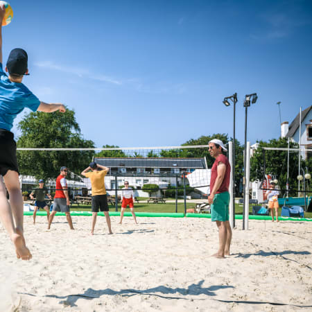 Joueur de volley-ball sautant pour frapper le ballon sur un terrain de sable à Bénodet-Glénan, avec d'autres participants et filets en arrière-plan