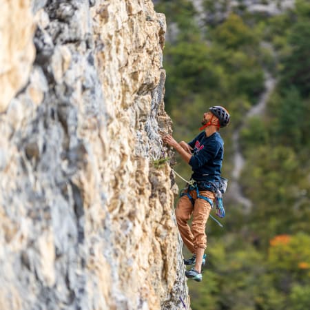 Grimpeur en escalade sur paroi rocheuse équipé de casque et harnais, développant autonomie et technique en plein air
