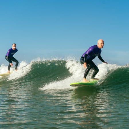 Deux surfeurs en combinaison chevauchant des vagues en Bretagne lors d'une session de coaching de surf