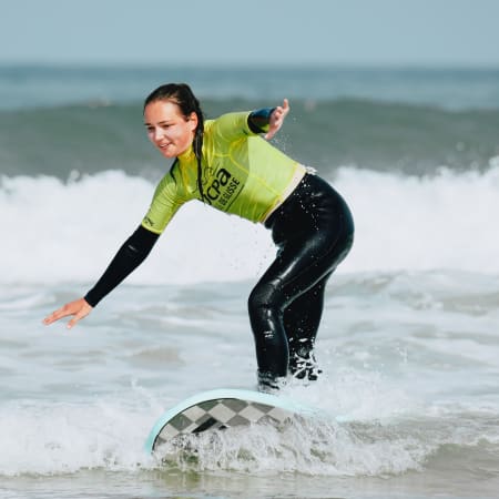 Surfeur en combinaison jaune et noire glissant sur une vague aux Landes avec technique équilibrée