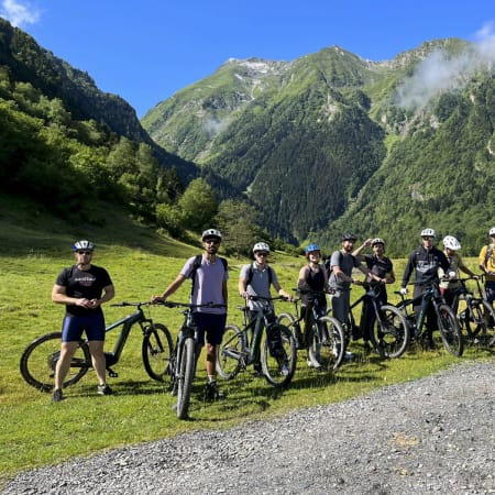 Groupe de cyclistes en stage d'apprentissage VTT dans une vallée des Pyrénées avec montagnes boisées en arrière-plan