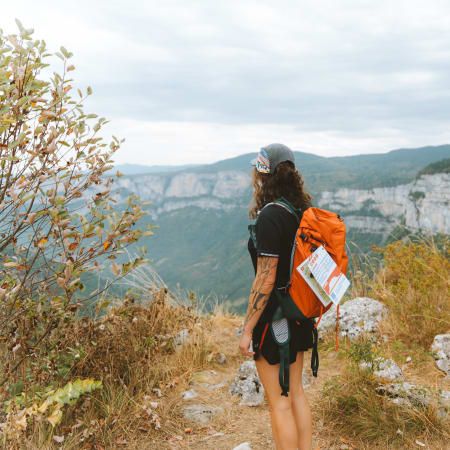 Randonneuse avec sac à dos orange face aux falaises spectaculaires du massif du Vercors