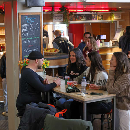 Intérieur animé d'un bar-restaurant des Arcs avec clients assis à des tables, comptoir de service et menu affiché