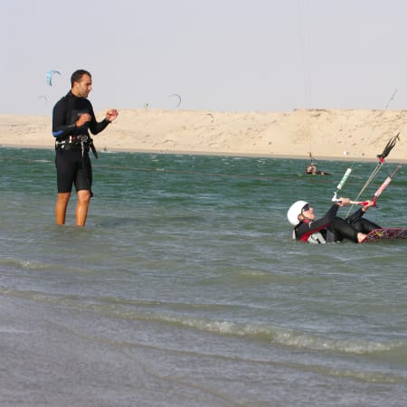 Débutant en kitesurf pratiquant dans un lagon avec moniteur, planche et voile en eau peu profonde