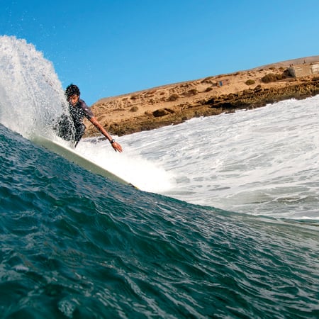 Surfeur sur une vague parfaite à Taghazout avec côte rocheuse marocaine et ciel bleu
