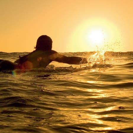 Surfeur pagayant sur sa planche au coucher de soleil lors du surf trip à Taghazout et Imsouane