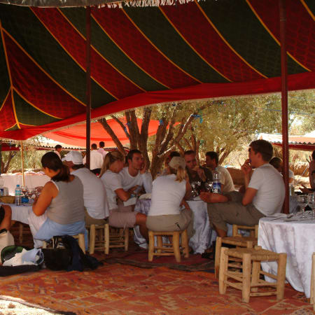 Marché traditionnel sous tente rouge dans une ville impériale marocaine avec vendeurs et visiteurs assis à des tables en bois