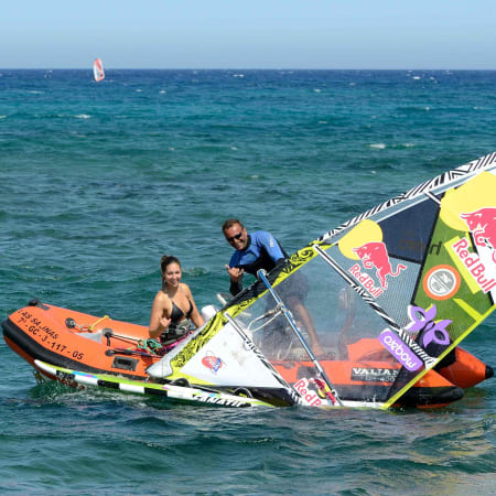 Windsurfeur et instructeur en mer avec voile colorée et planche de windsurf dans une baie aux eaux turquoise
