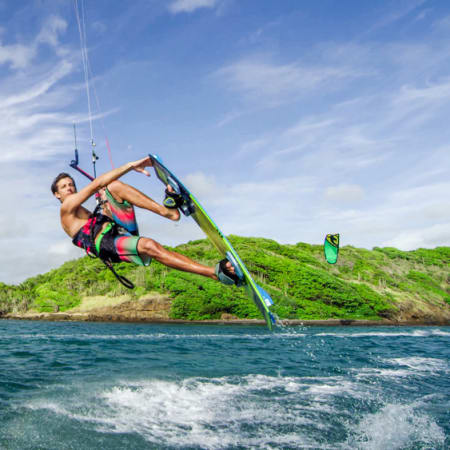 Kitesurfeur en action avec voile verte sur les eaux turquoise de la Martinique avec côte verdoyante en arrière-plan