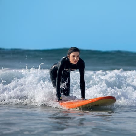 Surfeur en combinaison noire avec planche orange navigant dans les vagues de La Torche