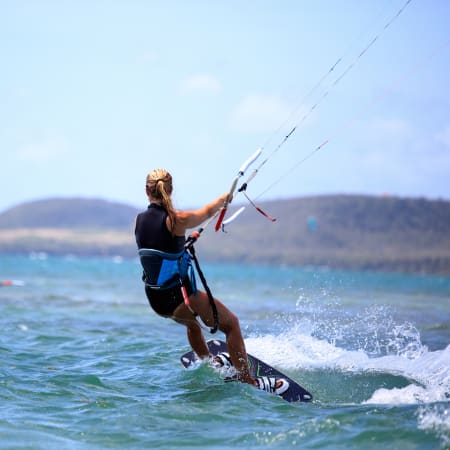 Kitesurfeur en action sur l'eau turquoise de Martinique avec groupe d'apprentis en arrière-plan et lagon du Vauclin