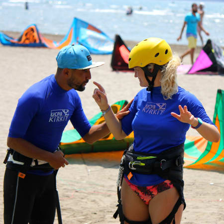 Moniteurs de kitesurf en équipement de sécurité discutant sur la plage avec cerfs-volants colorés et autres stagiaires en arrière-plan