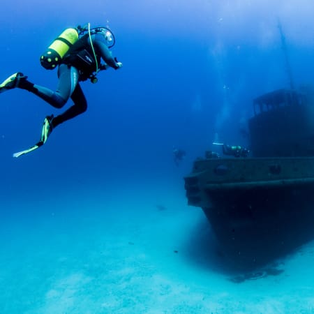 Plongeur en équipement complet explorant une épave sous-marine dans une eau turquoise cristalline