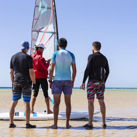 Groupe de windsurfeurs sur la plage préparant leur matériel avec voile colorée et planche avant de prendre la mer
