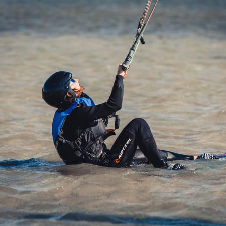 Kitesurfeur débutant assis dans le lagon peu profond tenant sa barre de contrôle, équipé d'un casque et d'une combinaison de protection
