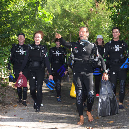 Groupe de plongeurs en combinaison noire et équipement de plongée marchant vers la plage pour débuter une formation sous-marine à Saint-Pierre