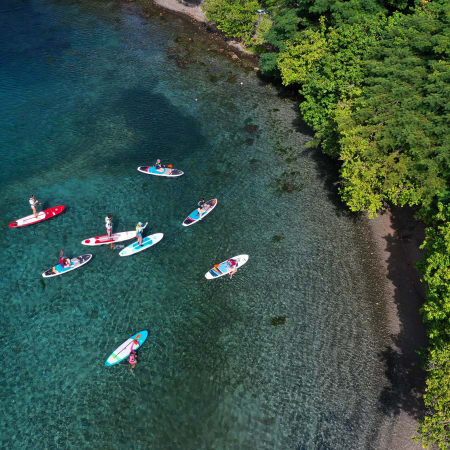 Vue aérienne de l'Archipel des Saintes avec paddleboards et kayaks dans les eaux turquoise bordées de végétation tropicale luxuriante