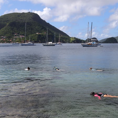 Baignade et snorkeling aux Saintes avec voiliers ancrés, îles verdoyantes et eaux turquoise