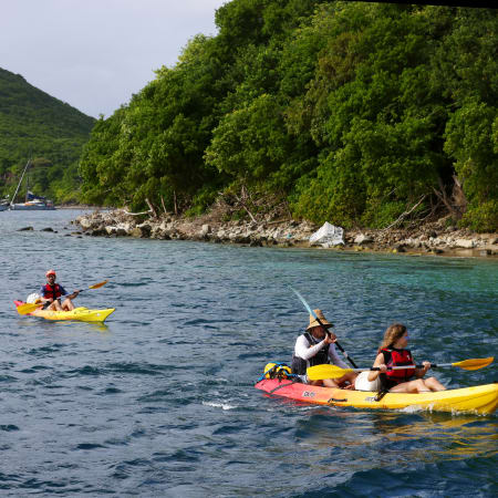 Kayak aux Saintes en Guadeloupe avec végétation tropicale luxuriante et voiliers en arrière-plan