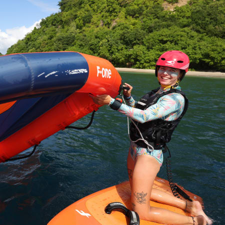 Participant en kitesurf aux Saintes avec voile rouge et bleue, îles verdoyantes et eaux turquoise en arrière-plan