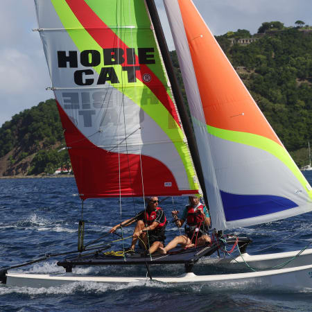Catamaran avec voiles colorées naviguant en baie des Saintes aux Antilles, îles verdoyantes en arrière-plan