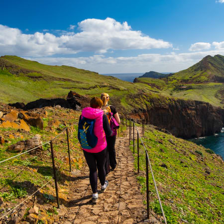 Randonneuse en gilet rose sur sentier côtier des Balcons de l'Atlantique avec falaises et océan bleu