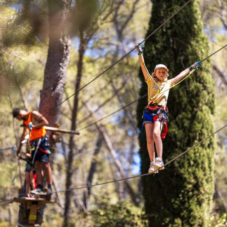 Jeune participant en tyrolienne équipé de harnais dans un parcours acrobatique en forêt, activité multisports pour école de pilotage