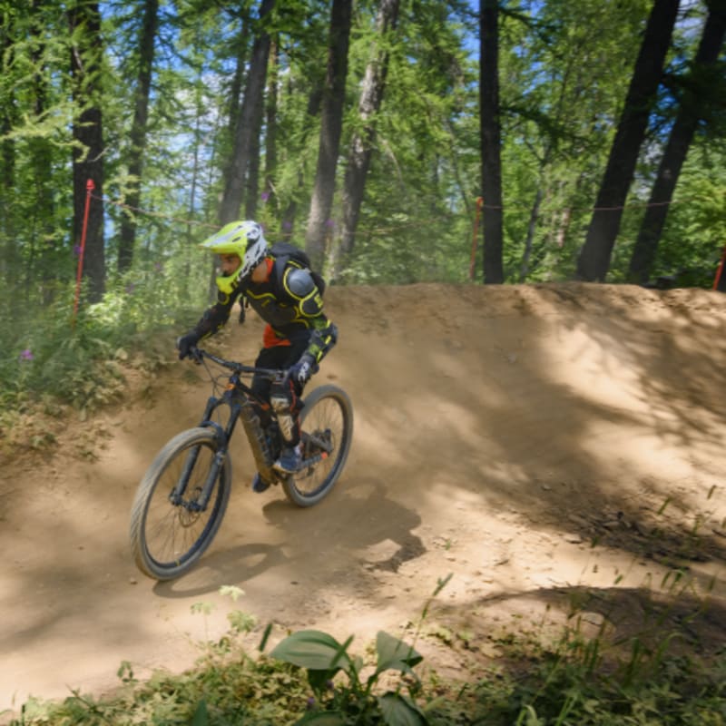 Jeune rider en VTT descente sur un sentier de terre aux Arcs avec casque et équipement de protection en forêt