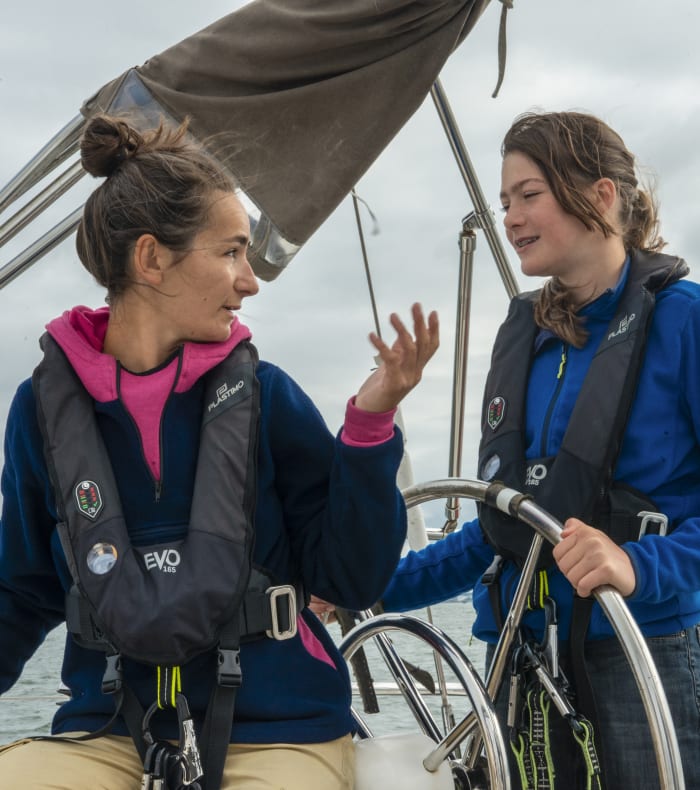Deux navigatrices en formation voile à la barre d'un voilier en Bretagne, portant gilets de sauvetage et vêtements de navigation