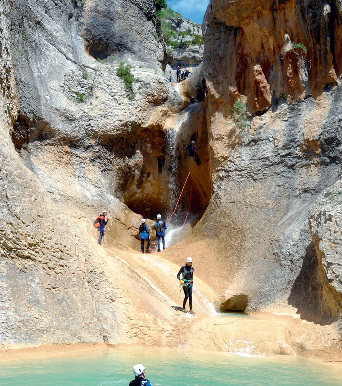 Groupe de canyoneurs en rappel dans une gorge rocheuse avec cascade d'eaux vives et parois de pierre